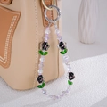 Elegant purple beaded phone strap with floral charms attached to a beige handbag - Purple