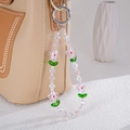 Pink floral beaded phone strap with green leaf accents hanging on a leather handbag - Pink
