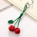 Detail of handmade cherry phone charm with red woven fruit and green leaves attached to a bag - Red
