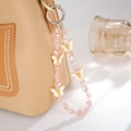 Dettaglio del lussuoso cinturino in cristallo con farfalle dorate su una borsa - Ciondolo Farfalla Rosa con Perline / Rosa