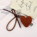 Close-up of caramel plush heart bag charm with bow strap and silver heart-shaped clasp - Dark Brown