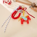 Macro shot of red faux leather flying horse bag charm with woven rope and pearl chain detail - Red