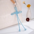 Detail of light blue woven leather knot bag charm with long tassels on a beige tote bag - Blue