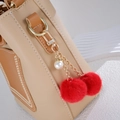 Close-up of fluffy red pom-pom keychain with pearl charm on khaki leather handbag detail - Charm / Red