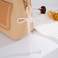 Detail of leather bag with white woven knot charm and neat stitching on beige and brown sides - White