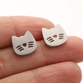 Detalle de pendientes de gato plateados con recorte de corazón sostenidos por los dedos - Estilo Gato (661) / Color acero
