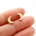 Detailed close-up of tiny gold moon stud earrings shown on fingertip for scale - Gold