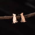 Pendientes de silueta de perro en oro rosa presentados sobre una rama natural - Estilo Perro Lobo (779) / Rosa oro
