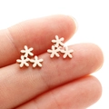 Three linked daisy stud earrings in rose gold finish held on a fingertip for scale - Rose Gold