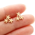 Detailed close-up of small golden triple flower stud earrings held on a fingertip - Gold