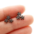 Close-up of matte black stainless steel triple daisy flower stud earrings on fingertip - Black