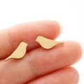 Macro shot of gold bird-shaped stainless steel earrings held on fingertips - Gold
