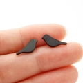 Detailed view of matte black bird stud earrings held by fingertips to show small size - Black