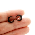 Macro shot of matte black crescent moon stud earrings held between fingers on white background - Black