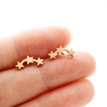 Gros plan détaillé de boucles d'oreilles étoiles triples en acier doré à la main - Or rose