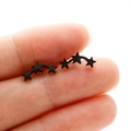 Gros plan de boucles d'oreilles étoiles noires mates tenues entre les doigts pour la taille - Noir