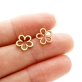 Detailed close-up of a tiny gold hollow flower earring held between fingers for scale - Gold