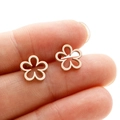 Detailed view of miniature rose gold hollow flower stud earrings held on a finger - Rose Gold