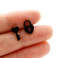 Macro shot of black stainless steel heart key and lock stud earrings held by hand - Black