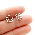 Macro shot of minimalist hollow flower stud earrings held on fingertip to show mini size - Steel