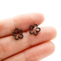 Close-up of minimalist black cutout flower stud earrings showing tiny scale on finger - Black