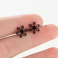 Primer plano de aretes de copo de nieve negros con diseño hueco entre los dedos - Negro