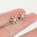 Detalle de los mini pendientes de copo de nieve de acero inoxidable entre los dedos - Color acero