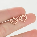 Gros plan de boucles d'oreilles cœur ajouré en or rose tenues à la main pour l'échelle - Or rose