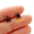 Detail view of 4mm black star stud earrings showing actual size held by fingers - 4mm / Black