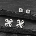 Polished silver stainless steel clover stud earrings with hollow design on rock background - Steel