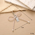 Pink beaded bow phone charm with pearls and silver coin tag on beige textured background - Pink Crystal Bowknot