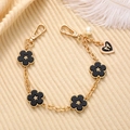 Detail of a gold-finish chain with black floral charms and a pearl on a beige fabric - Black
