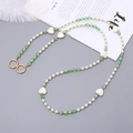 Détail de chaîne en perles et cristaux verts avec anneaux dorés sur un fond gris élégant - Vert