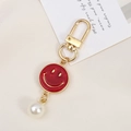 Detail view of a red enamel smiley face keychain with a white pearl and golden clasp - Faux Shell Smiley Style (K3612)
