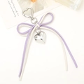 Close-up of purple and beige leather bow charm with silver heart pendant and heart-shaped clasp - White + Purple