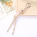 Detail of hand-woven 6mm leather cord keychain with silver spring clip and metal caps - Off-white