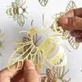 Pegatinas de pared de abejas huecas doradas cortadas con láser mostradas en mano - Abeja Dorada