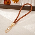 Detailed close-up of brown woven leather phone strap with polished gold metal clasp - Charm / Brown