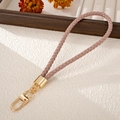 Detail of hand-woven dust pink PU leather phone strap with golden lobster clasp and hardware - Charm / Pink