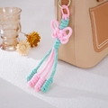 Detail eines rosa-grün handgewebten Schleifenanhängers an einem beigen Handtaschengriff - Rosa