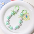Detail of colorful gradient mermaid beads with cute bear and bow charms on white plate - Green + White