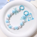 Detail of beaded bear keychain with blue bow and mermaid beads on white plate - Blue and White