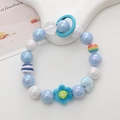Detail of light blue beaded phone strap with flower charm and rainbow beads on white stand - Blue Flower