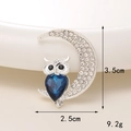 Macro shot of silver owl on crescent moon brooch with blue crystal heart and rhinestones - Silver Moon Owl