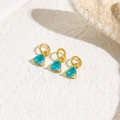 Detailed macro view of gold-plated triangle pendants with light blue zircon on white sand - Lake Blue