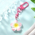 Close-up of a pink frangipani flower keychain with yellow center on a blue wave background - Pink