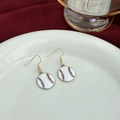 Detailed close-up of baseball bow earrings with red stripes and gold hooks on ceramic - Round Baseball Drops