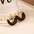 Detail of gold metal earrings with brown flocked rings hanging on a white ceramic cup - Brown