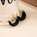 Detail of gold metal and black velvet U-shaped hoop earrings on a white ceramic cup - Black
