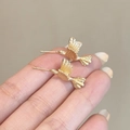 Dettaglio di piccoli orecchini a lobo a forma di colibrì dorati tra i polpastrelli - Design Fenice (E1936)